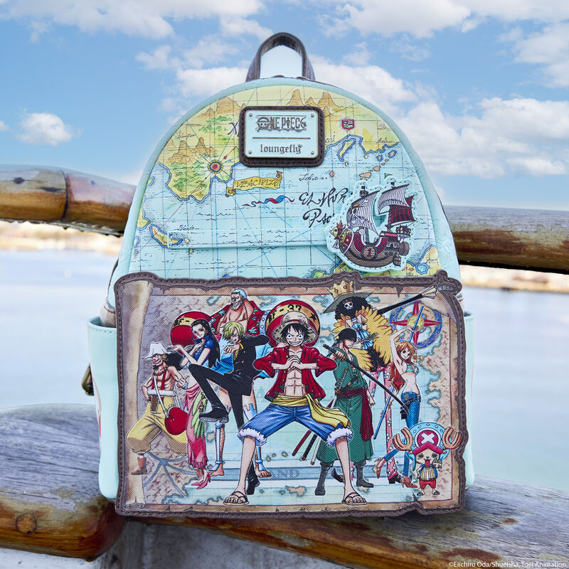 Loungefly One Piece 25th anniversary mini backpack sitting on a rock at the beach, showing off a map design on the mini backpack and the Straw Hat Pirates Luffy, Chopper, Nami, Usopp, Sanji, Robin, Brook, Zero, and Franky on the front pocket 